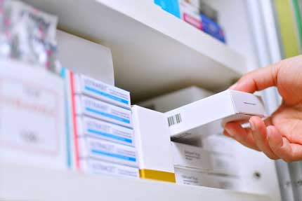 a hand pulling medication from a pharmacy shelf