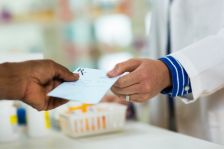 A person is passing prescription paper to pharmacist