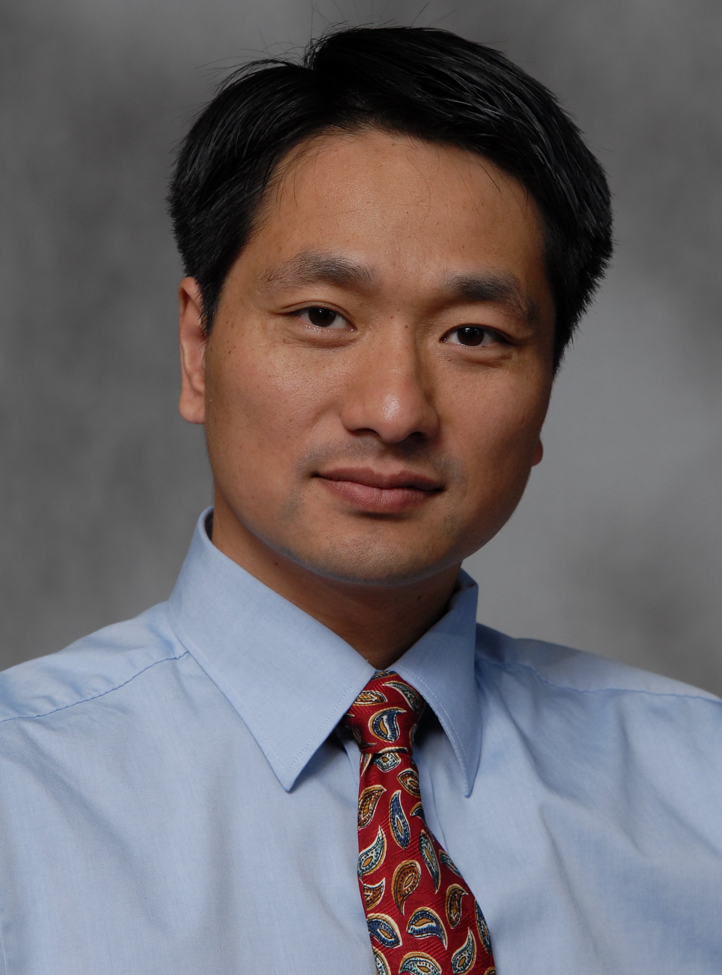 Headshot of Dr. Changquan Calvin Sun wearing a light blue collared shirt and red tie.