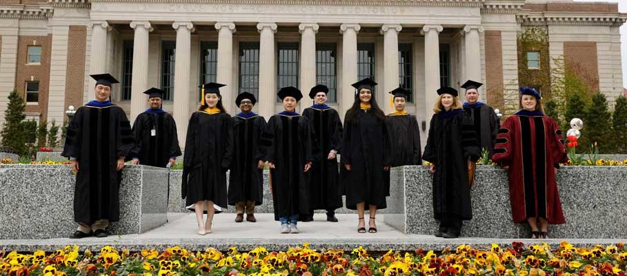 Graduate students and directors, in regalia, standing in front of the Northrup building