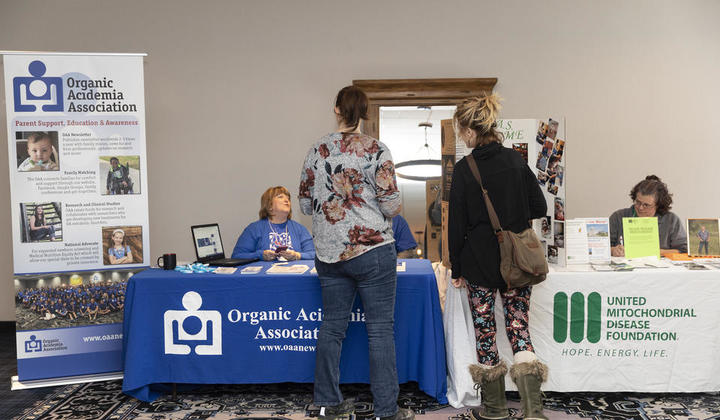 Attendees interacting with representatives from the Organic Acidemia Association and the United Mitochondrial Disease Foundation