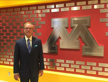Bill Larson standing in front of red and gold UMN wall